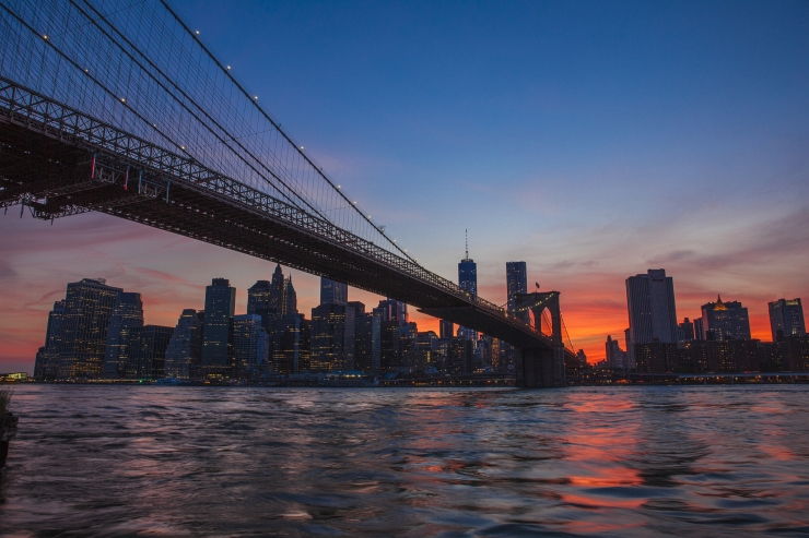 The Brooklyn Bridge stretches towards Manhattan and a beautiful sunset